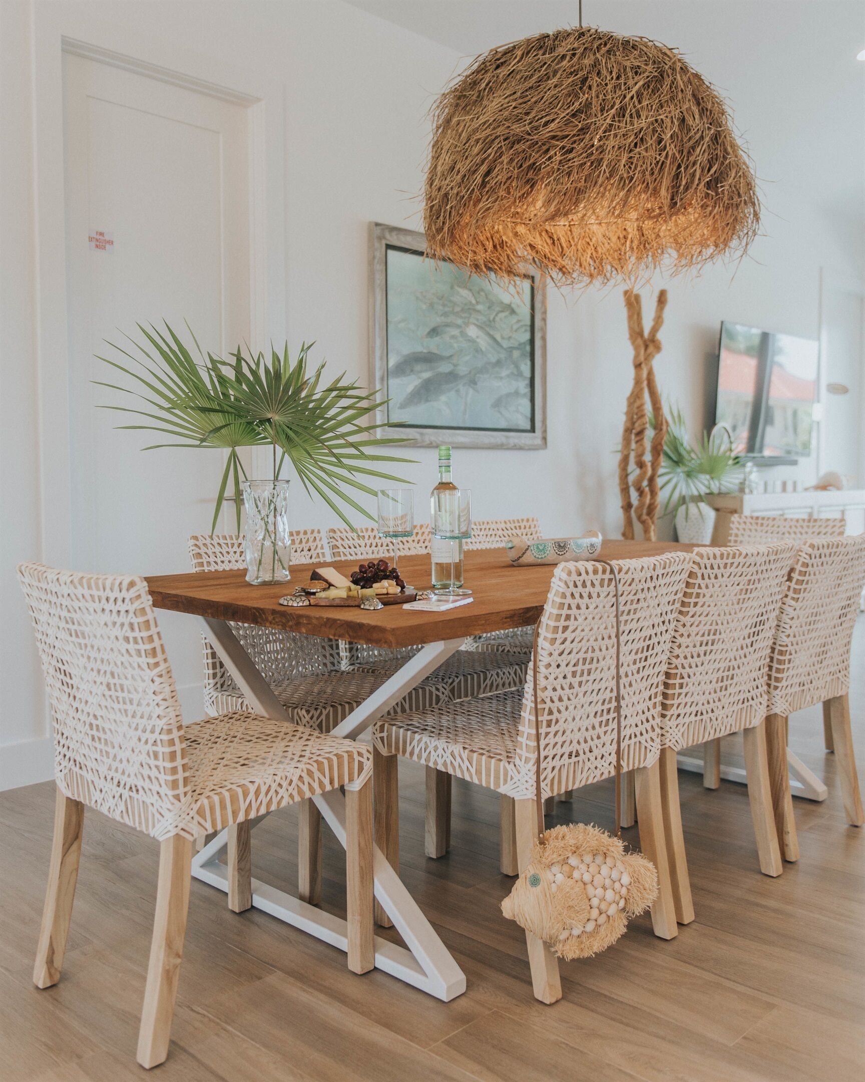 A dining area with a wooden table, wicker chairs, a hanging basket light, and a framed picture on the wall.