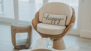 A wicker chair with a cushion labeled "happy" and a small wooden stool. - Modern Island Luxury | 4 En-Suite Masters, 6 BA, Pool, Dock & Outdoor Oasis (Key Colony Beach)