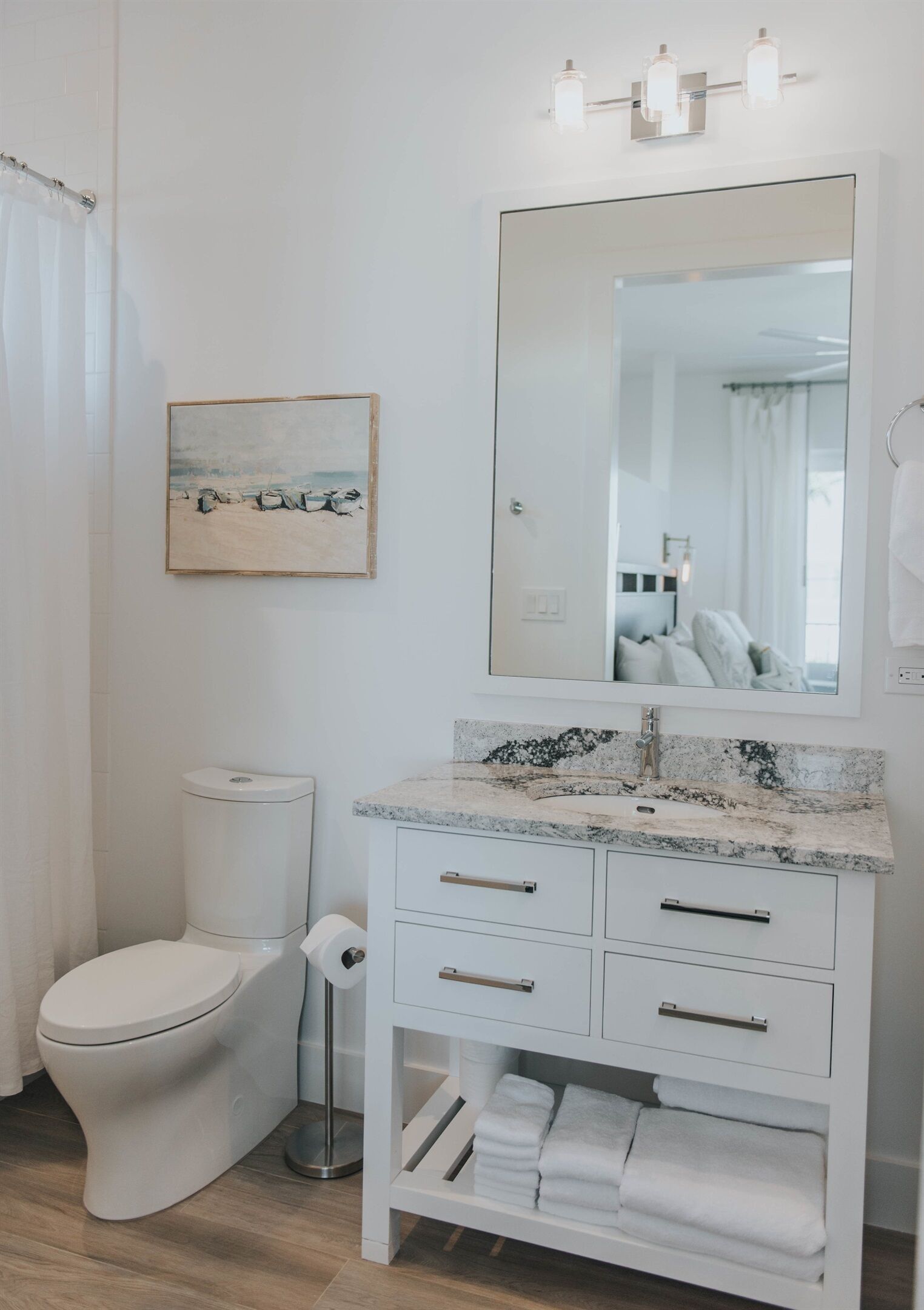 A bathroom with a white toilet, a sink with a marble countertop, a large mirror, and a framed picture on the wall.