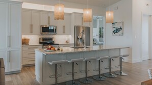 A modern kitchen with white cabinets, stainless steel appliances, a central island with bar stools, and pendant lighting. - Modern Island Luxury | 4 En-Suite Masters, 6 BA, Pool, Dock & Outdoor Oasis (Key Colony Beach)