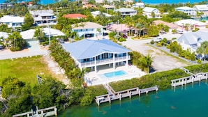 A large house with a swimming pool, surrounded by a dock and lush greenery. - Modern Island Luxury | 4 En-Suite Masters, 6 BA, Pool, Dock & Outdoor Oasis (Key Colony Beach)