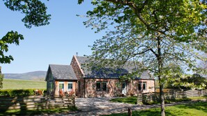 Une maison en pierre avec un toit en pente, une clôture en bois et une pelouse verdoyante.