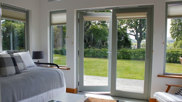 Une chambre à coucher comprenant un lit, une table de chevet, une chaise et donnant sur un jardin grâce à une porte-fenêtre coulissante.