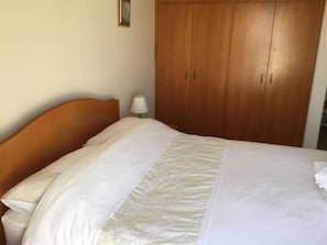 Un lit bien fait, avec du linge de lit blanc et une tête de lit en bois.
