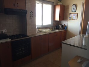 Une cuisine avec des meubles de rangement en bois, une cuisinière, un évier et une fenêtre avec des stores.