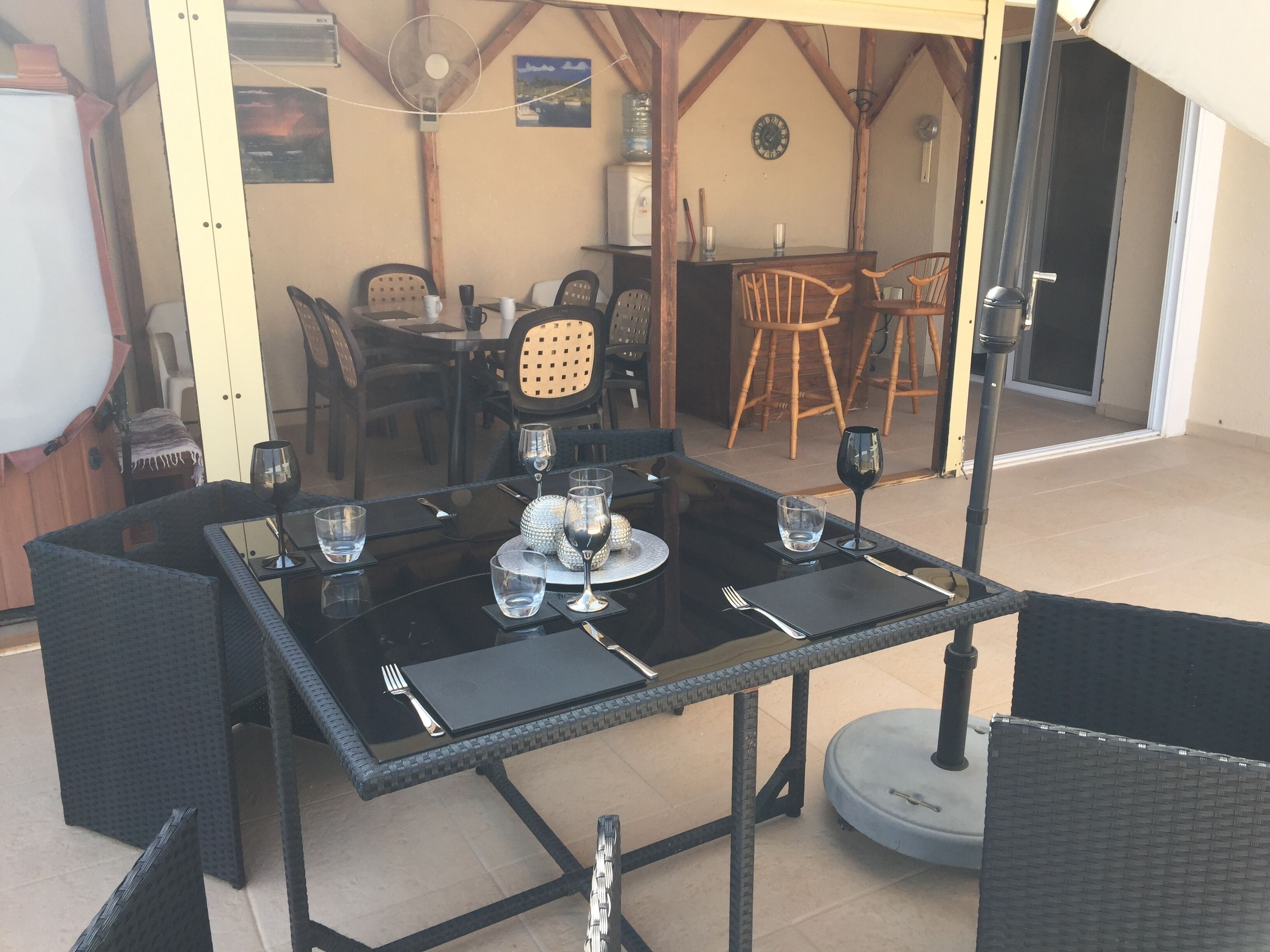 Un espace de restauration en plein air avec une table dressée pour quatre personnes, entourée de chaises en osier.