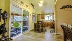A spacious kitchen with wooden cabinets, a dining area with a green chair, and a sliding glass door leading to a deck. - COZY HIDEAWAY IN THE OHIA RAINFOREST LOCATED BELOW VOLCANO NATIONAL PARK (Mountain View)