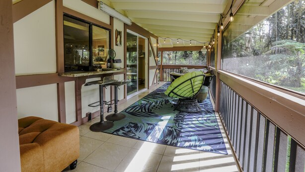 A covered outdoor area with a seating arrangement, a bar counter, and a view of the outdoors. - COZY HIDEAWAY IN THE OHIA RAINFOREST LOCATED BELOW VOLCANO NATIONAL PARK (Mountain View)