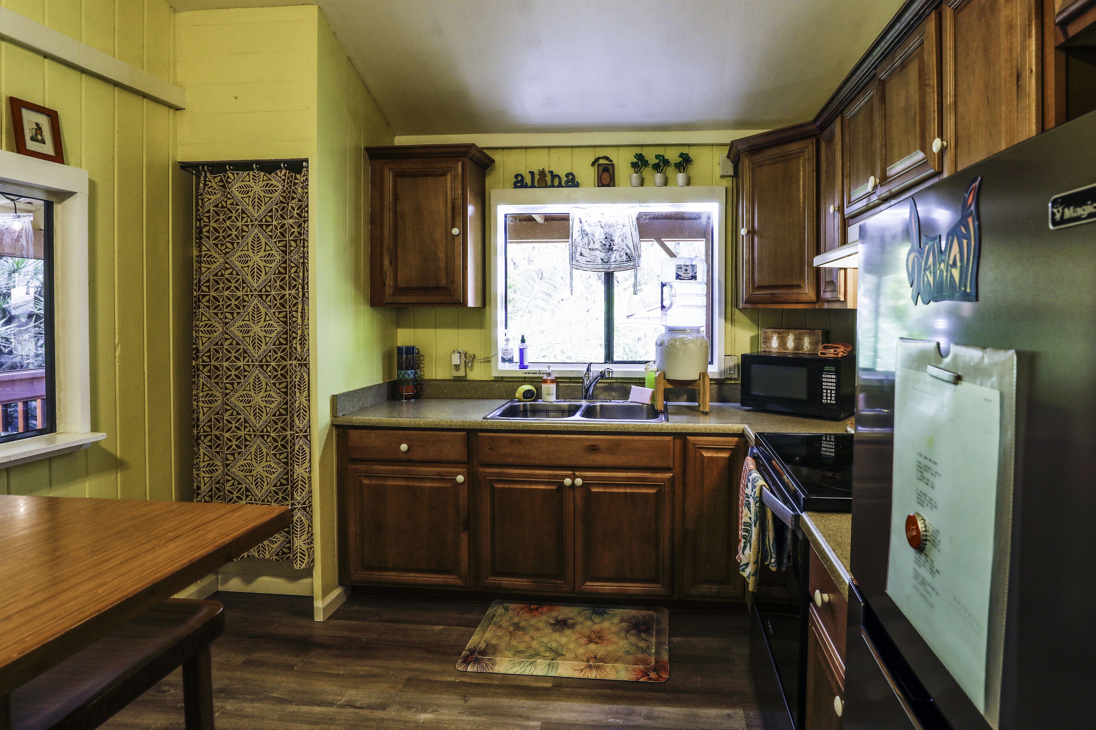 A kitchen with wooden cabinets, a stainless steel refrigerator, and a window with a view of the outdoors.