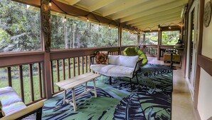 A covered porch with a wooden bench, a cushioned bench, and a patterned rug. - COZY HIDEAWAY IN THE OHIA RAINFOREST LOCATED BELOW VOLCANO NATIONAL PARK (Mountain View)