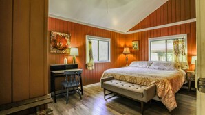 A bedroom with a bed, desk, chair, bench, and two windows with curtains. - COZY HIDEAWAY IN THE OHIA RAINFOREST LOCATED BELOW VOLCANO NATIONAL PARK (Mountain View)