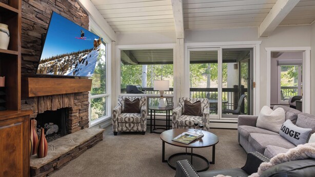 A cozy living room with a stone fireplace, comfortable seating, and a large TV displaying a snowy mountain scene. - Top of the Village~Ski-in/out~HT~Pool~Grill~Parking (Snowmass Village)