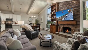 A modern living room with a fireplace, a television, and a dining area. - Top of the Village~Ski-in/out~HT~Pool~Grill~Parking (Snowmass Village)