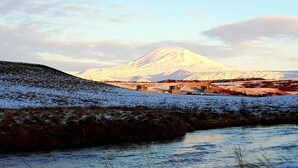 A snow-covered landscape with a river, a mountain in the background, and a small building with a red roof. - Afternoon Cottages near Hella, Hekla & Landmannalaugar (Hella)