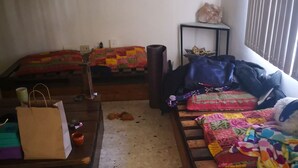 Ein Zimmer mit zwei Holzbetten, einem kleinen Tisch und einem Fenster mit Jalousien.