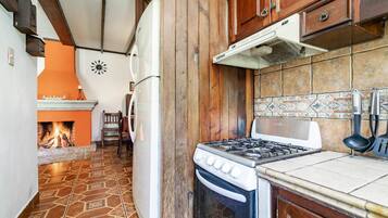 A kitchen with a gas stove, white refrigerator, and orange wall.