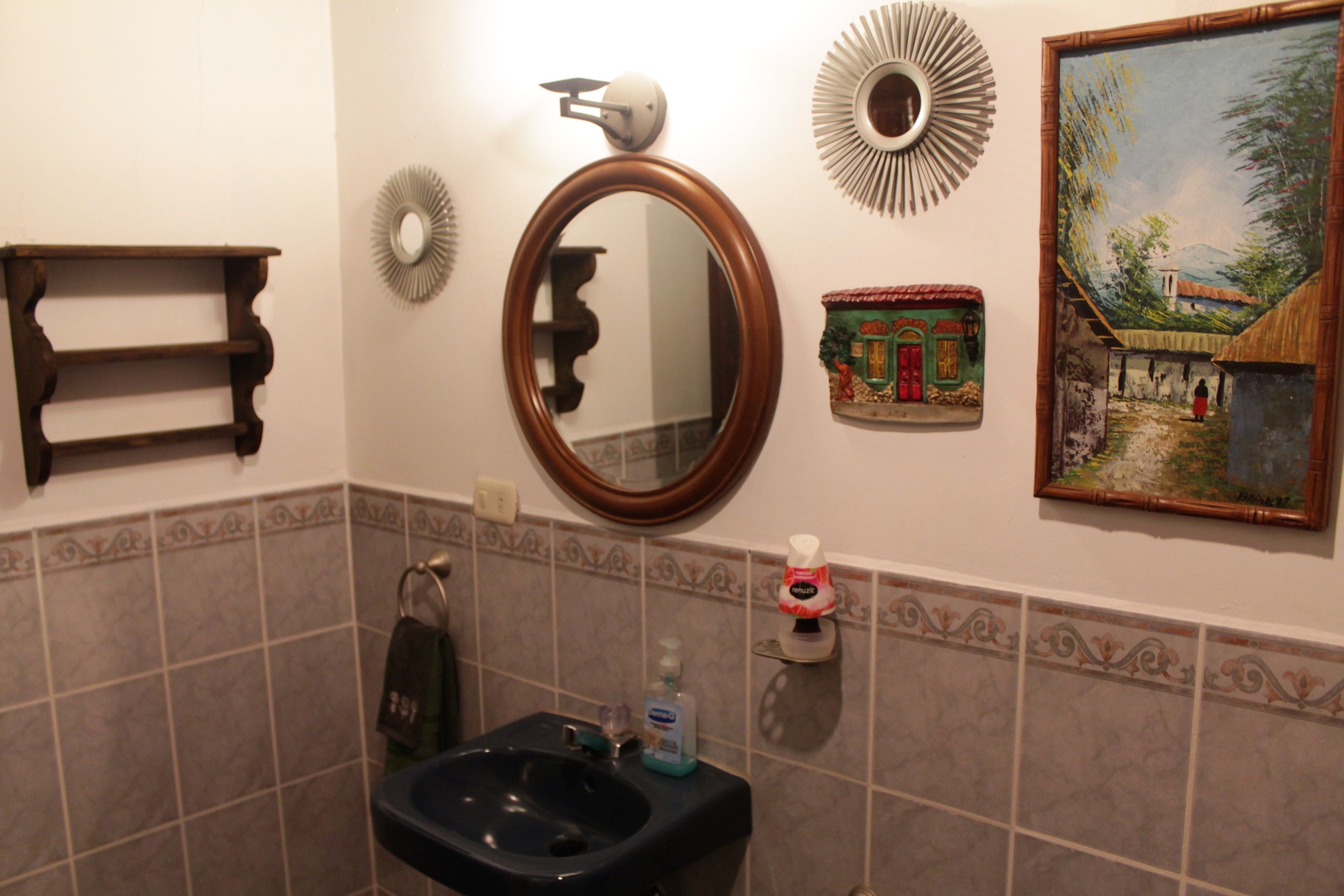 Une salle de bain comprenant un lavabo, un miroir, des carreaux décoratifs sur les murs, un porte-serviettes et un tableau encadré.