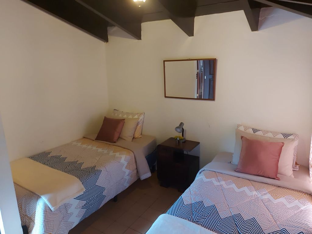 A small, cozy room with two single beds, a nightstand with a lamp, and a mirror on the wall.