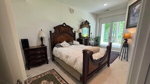 A bedroom with a large bed, a dresser, a nightstand, a mirror, and a window with a view of greenery. - NEW! Ft Marcy 2 BR 1 LV/DRM 1 BA on Pimmit Run, hike/ kayak to the Potomac River (McLean)