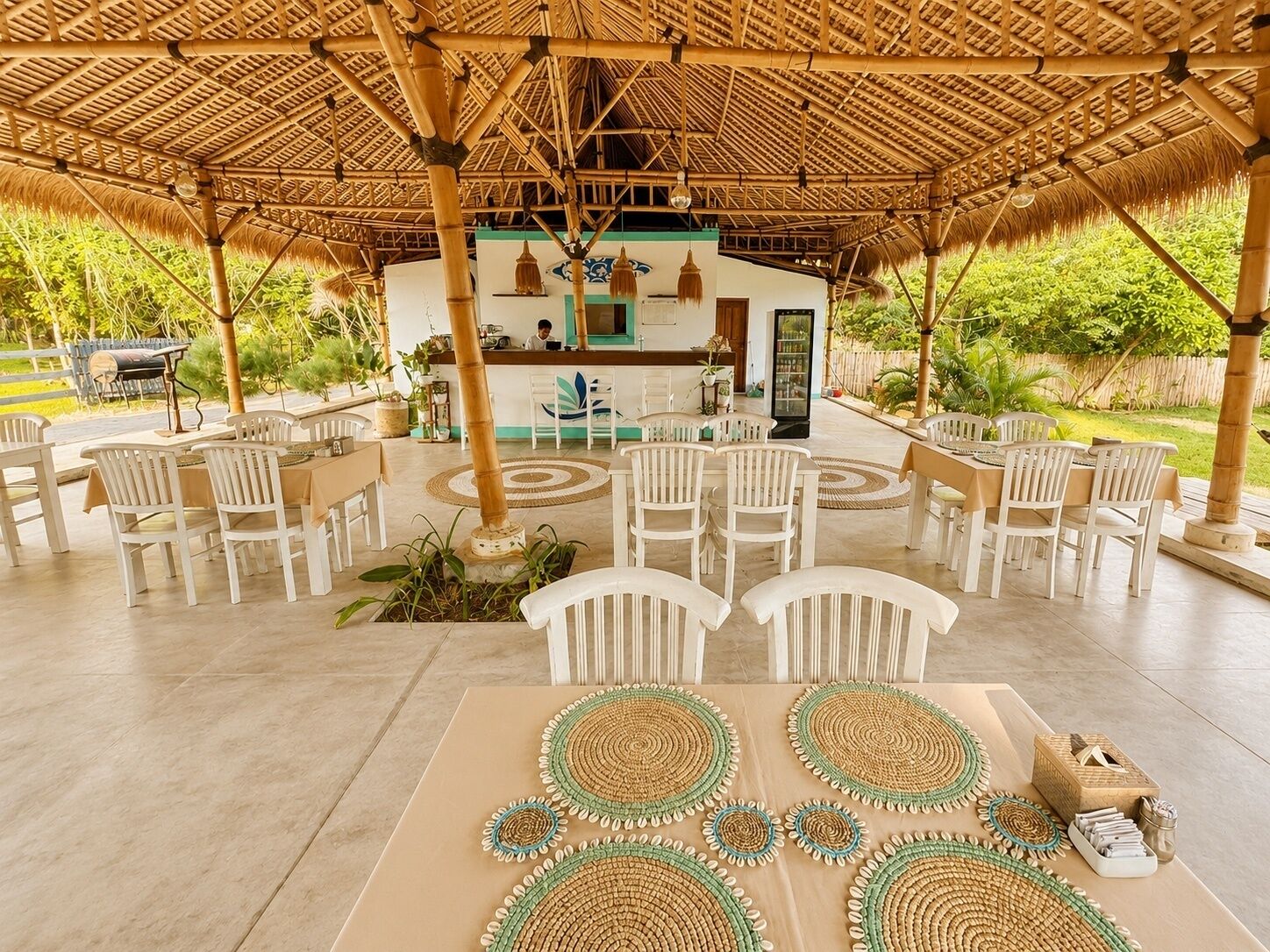 An outdoor seating area with white chairs and tables, a bamboo roof, and a view of a building with a green door.