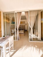 Una habitación con puerta de vidrio que da a un balcón, una cama con vistas y un comedor con mesa y sillas.