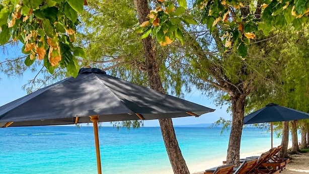 A beach with wooden lounge chairs and umbrellas, a sandy shore, and a clear blue sea. - Samalas Boutique Hotel resort & Private Pool Villas (Gili Meno)