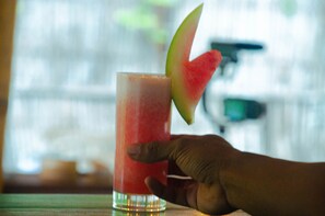 Una mano sostiene un vaso alto con una bebida roja y una tajada de sandía en el borde.