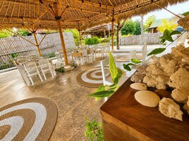 An outdoor seating area with tables and chairs, surrounded by plants and decorative mats.