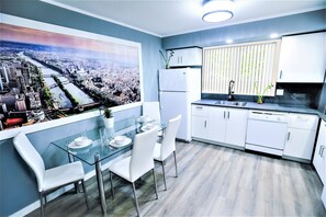 Una cocina moderna con armarios blancos, una mesa de comedor de vidrio y vistas a la ciudad.