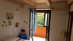 Et soveværelse med seng, et vindue med gardin, et lille bord med vase og vægdekorationer.