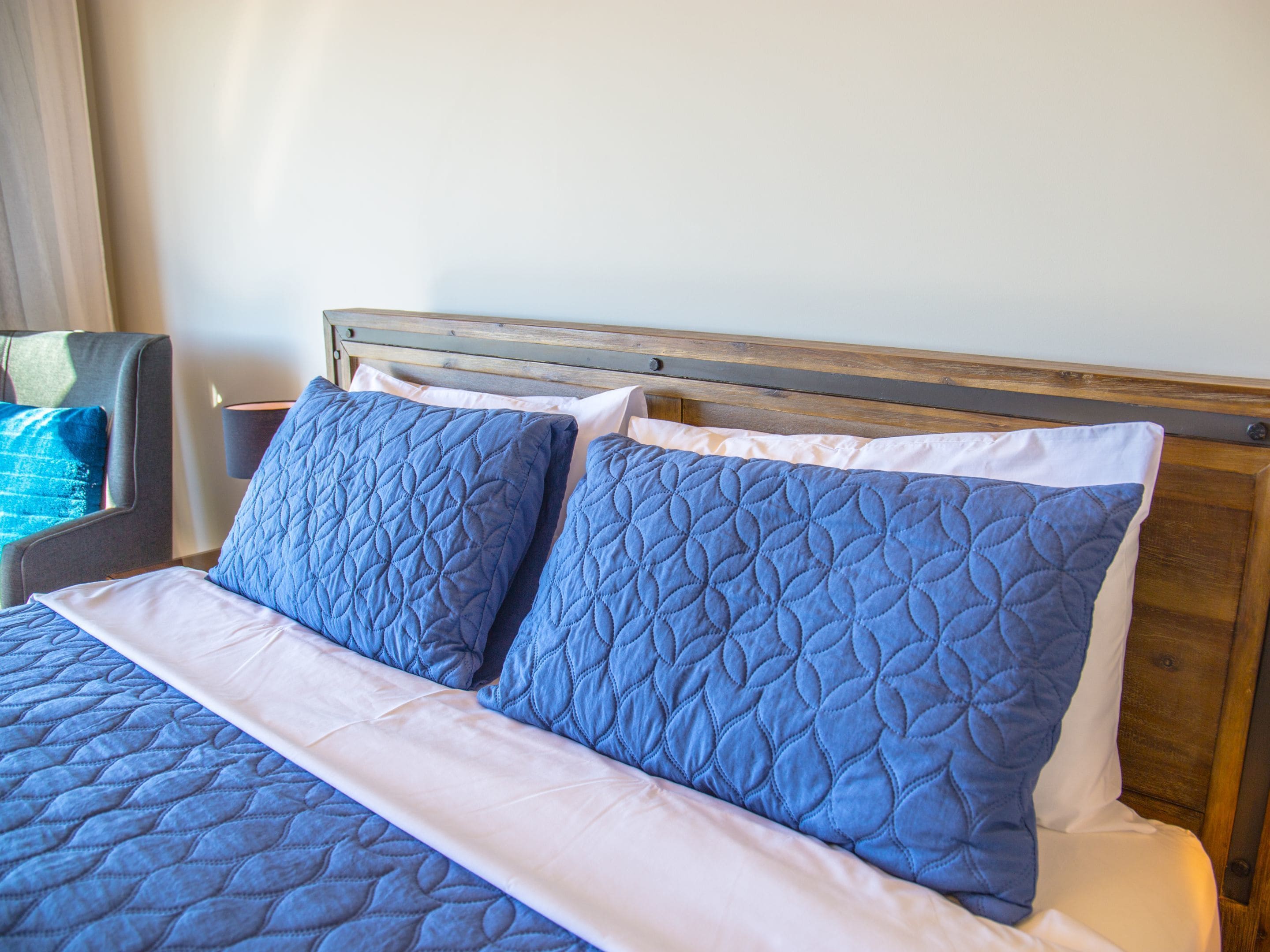 A bed with a wooden headboard, blue quilted pillows, and a white bedspread.
