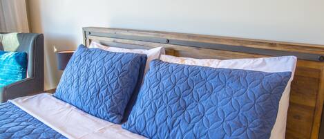 A bed with a wooden headboard, blue quilted pillows, and a white bedspread.