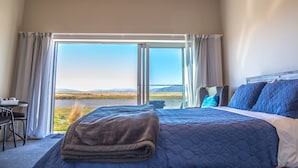 A bedroom with a large bed, a desk, and a view of a landscape through a sliding door.