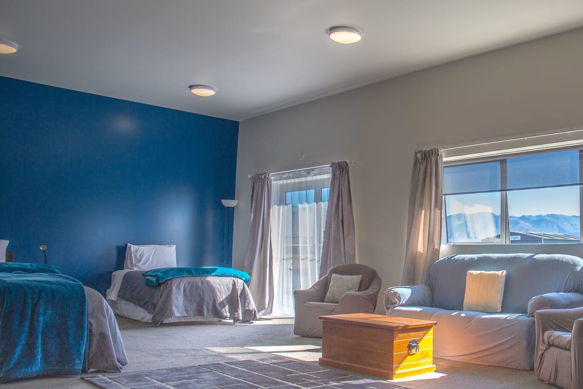 Une chambre moderne avec un mur d’accent bleu, un lit, un canapé, une commode et une fenêtre donnant sur les montagnes.