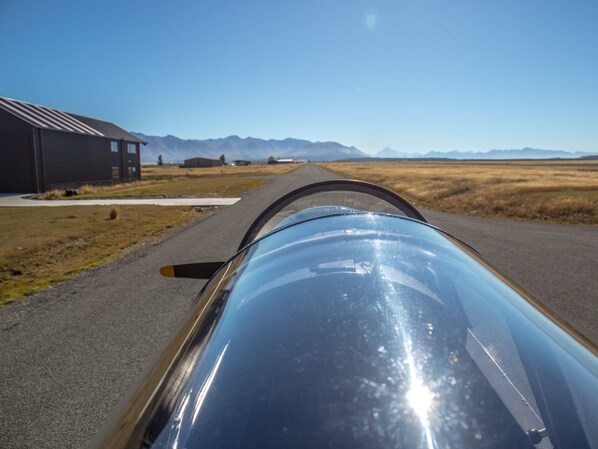 A vehicle's windshield with a clear view of a road, buildings, and distant mountains.