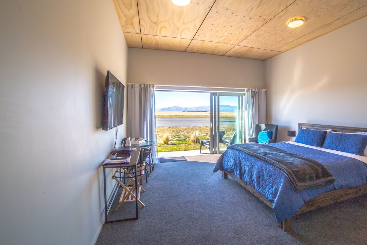 Une chambre à coucher avec un lit, un bureau, une chaise, un téléviseur et une vue sur l’extérieur.