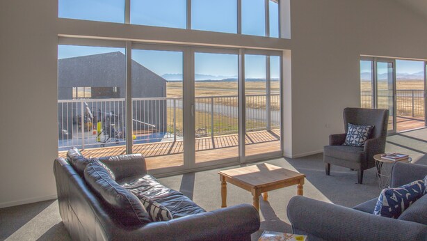 A spacious living room with large windows, a wooden deck, and a view of a distant landscape.