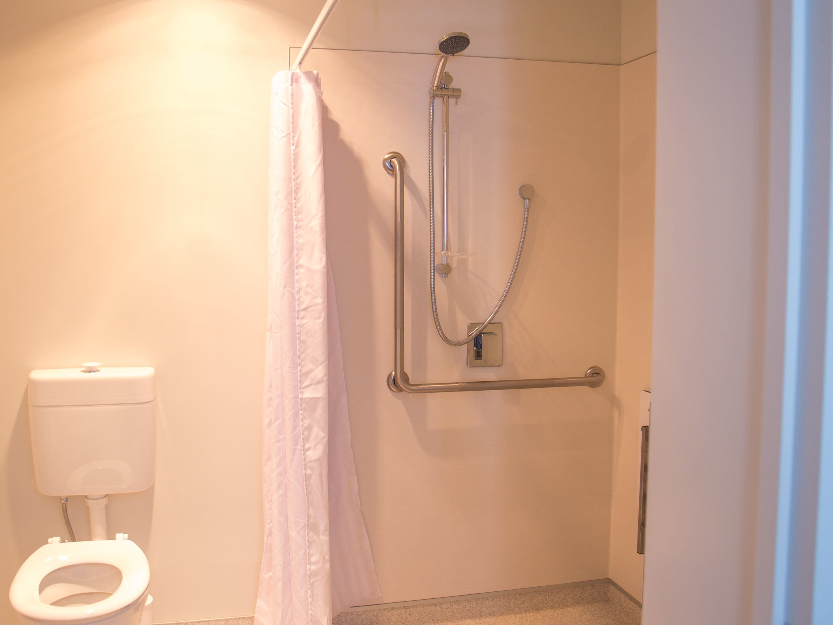 Un baño con ducha, inodoro y barra de apoyo.