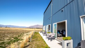 A large blue building with a patio area featuring outdoor seating and a view of a field and mountains.