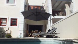 Un espace aménagé au bord de la piscine, avec des chaises longues, un parasol et une petite table.