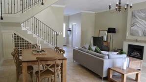 Un grand espace de vie comprenant un escalier, une table à manger avec des chaises, un canapé et une cheminée.