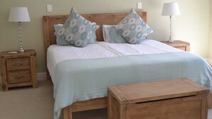 Un lit avec une tête de lit en bois, deux tables de chevet avec des lampes, un tiroir de chevet et un banc en bois.