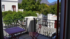 Un balcon agrémenté d’une table et de chaises, entouré d’une balustrade en fer forgé, d’où l’on peut admirer un paysage montagneux.