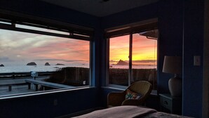 Une chambre avec une grande fenêtre donnant sur un coucher de soleil et la mer.
