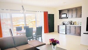 A living room with a sofa, a coffee table with a vase of flowers, a dining area with chairs, and a kitchen with appliances. - Stunning 2br/2 KING Beds / Spectacular View & Best Location - Expansive Balcony  (Cabo San Lucas)