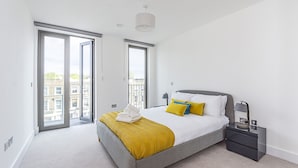 Un dormitorio moderno con una cama grande, una mesita de noche y vistas a la ciudad a través de una puerta corrediza.