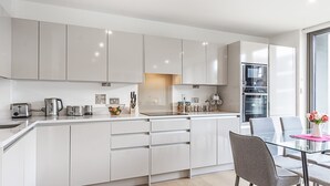 Una cocina moderna con armarios blancos, una mesa de comedor de vidrio y vistas de la ciudad a través de grandes ventanales.