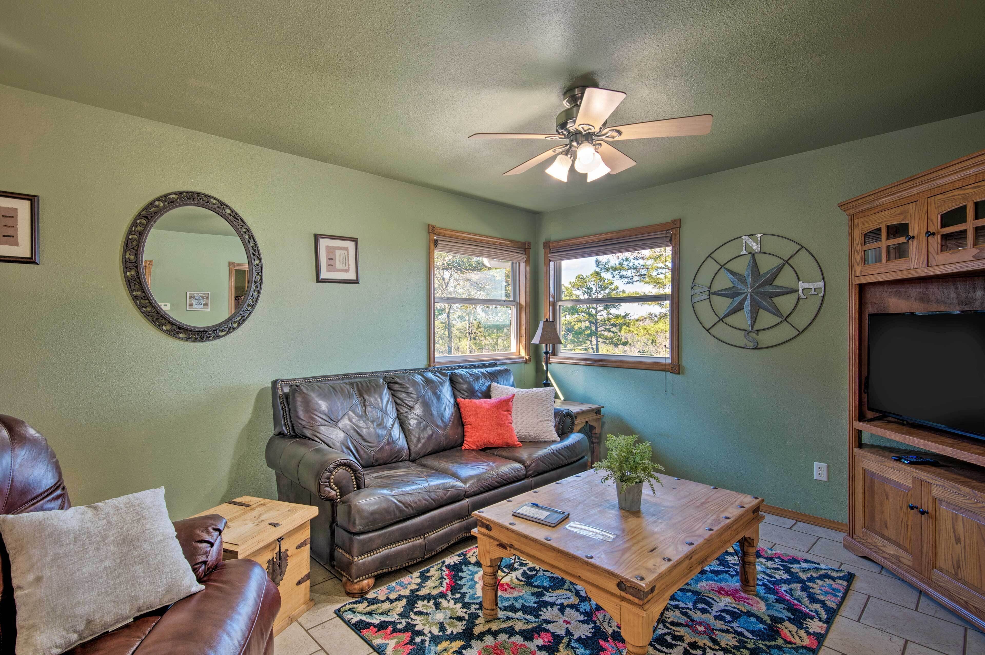 A living room with a brown leather couch, a wooden coffee table, a TV cabinet, and a ceiling fan.