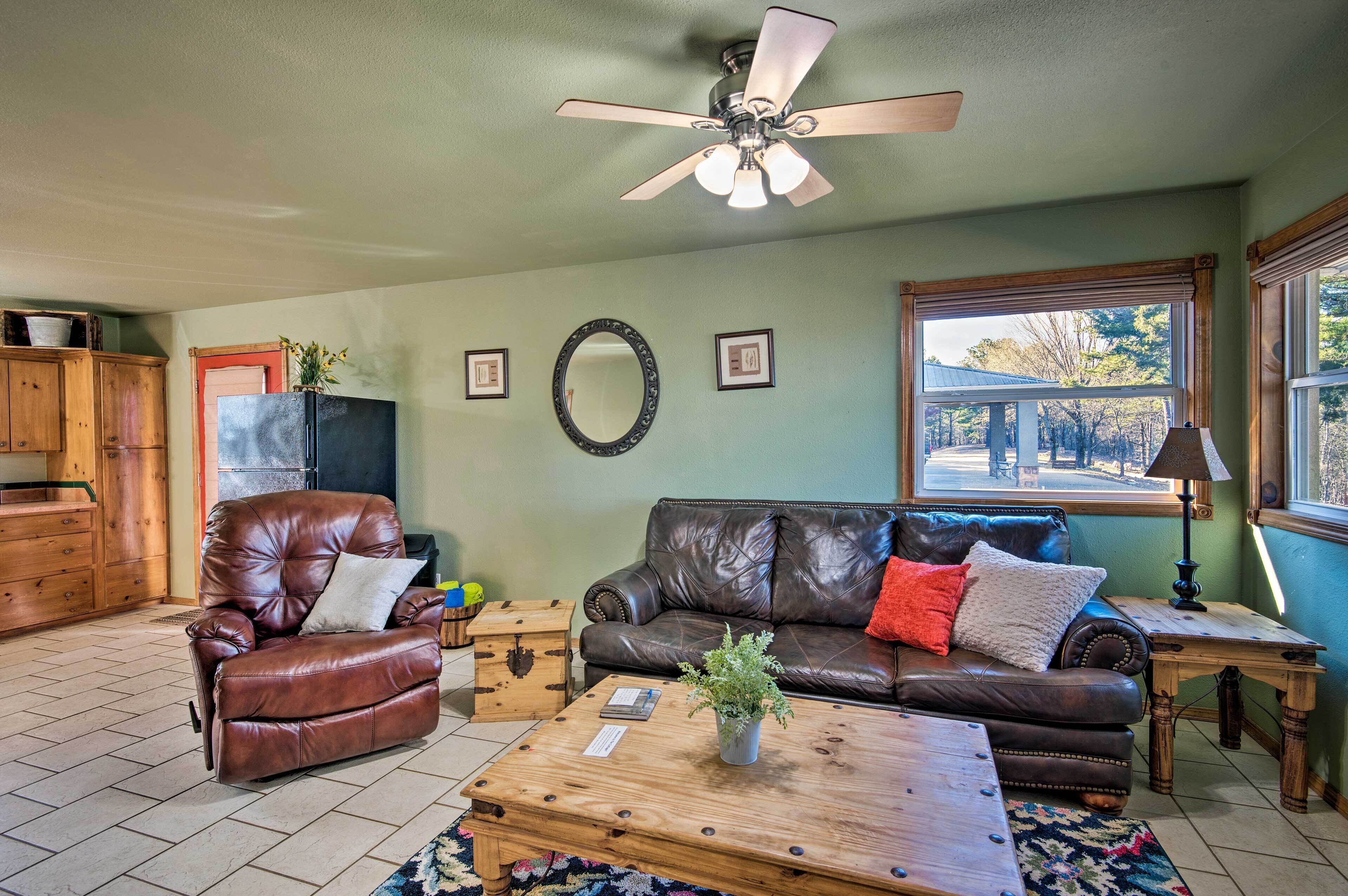A living room with a leather sofa, a leather armchair, a wooden coffee table, and a ceiling fan.