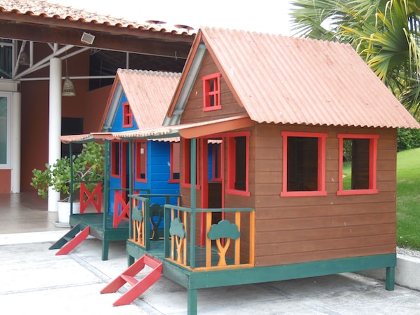A children's playhouse with a red roof and blue walls, featuring a slide and a small porch.